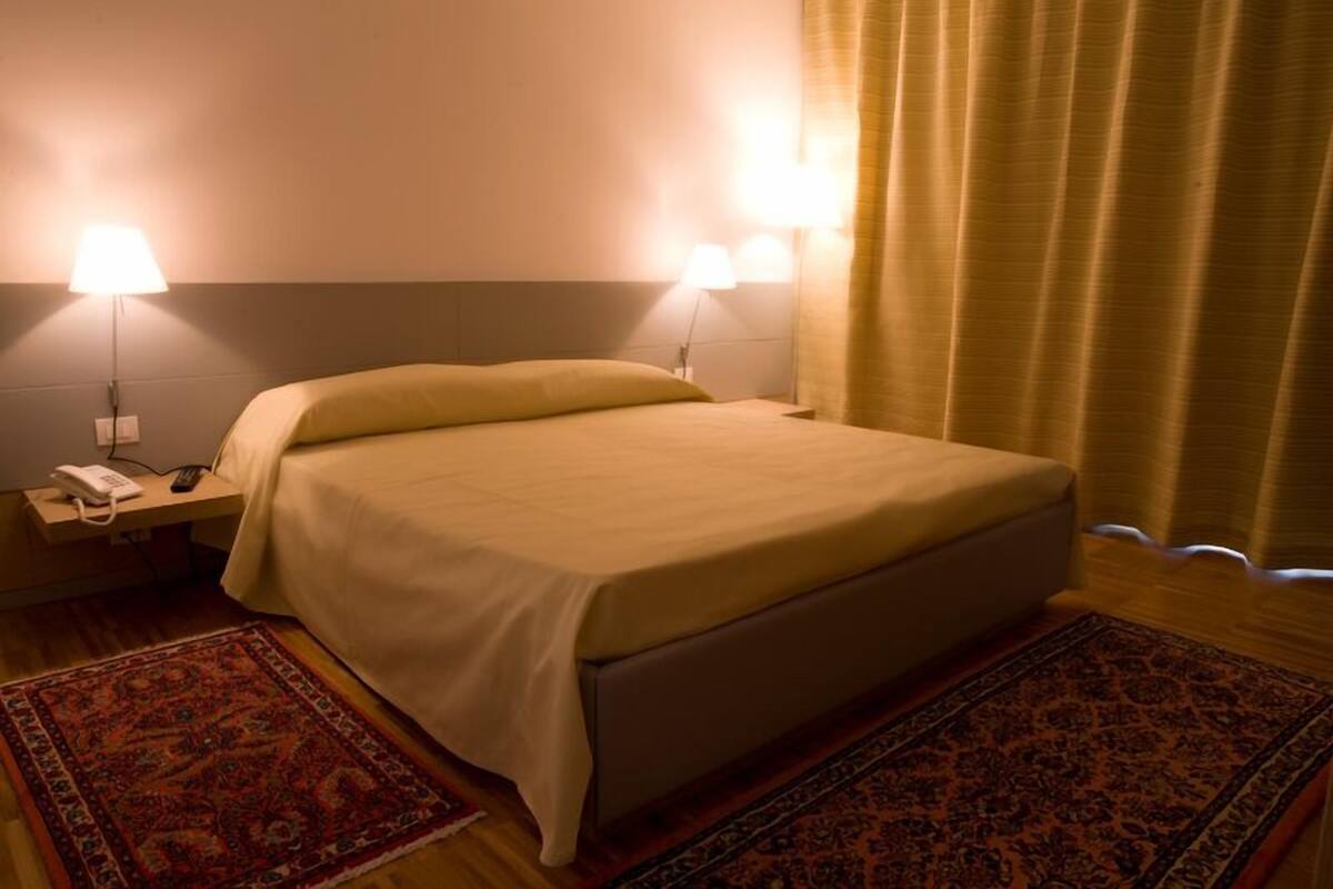 A hotel room with a bed, two bedside lamps, a telephone, and a patterned rug.