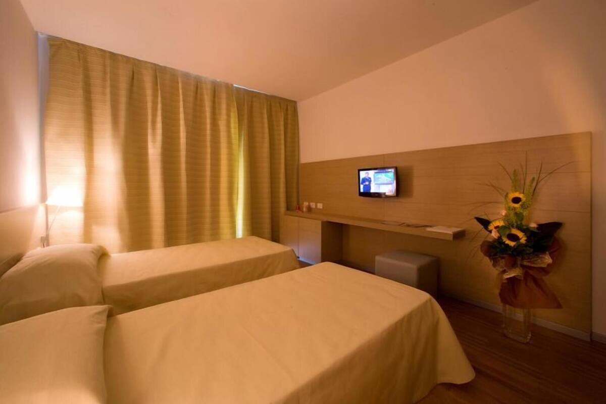A hotel room with two beds, a TV on the wall, and a bouquet of flowers.