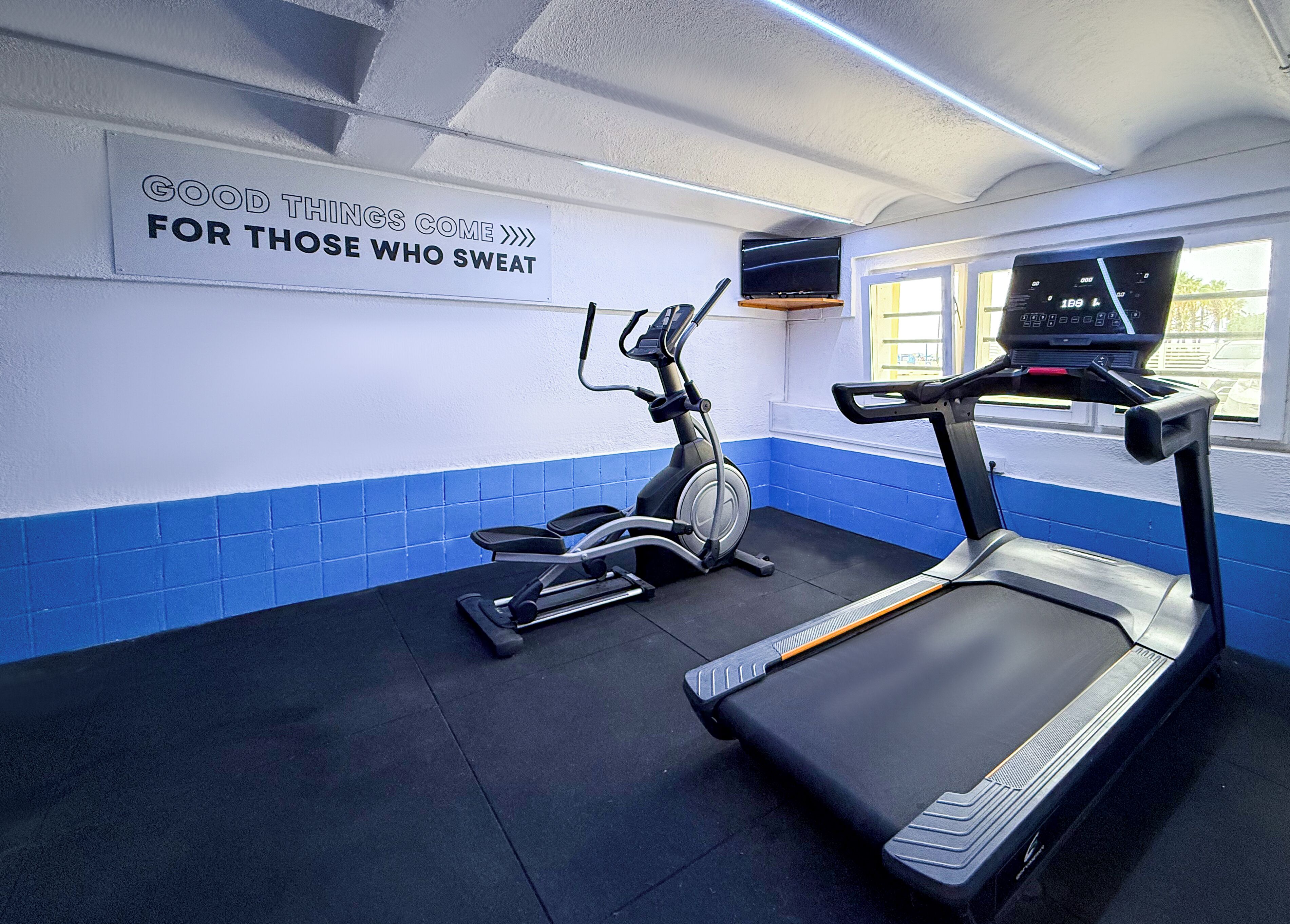 Ett gym med löpband, crosstrainer och en motiverande skylt på väggen.