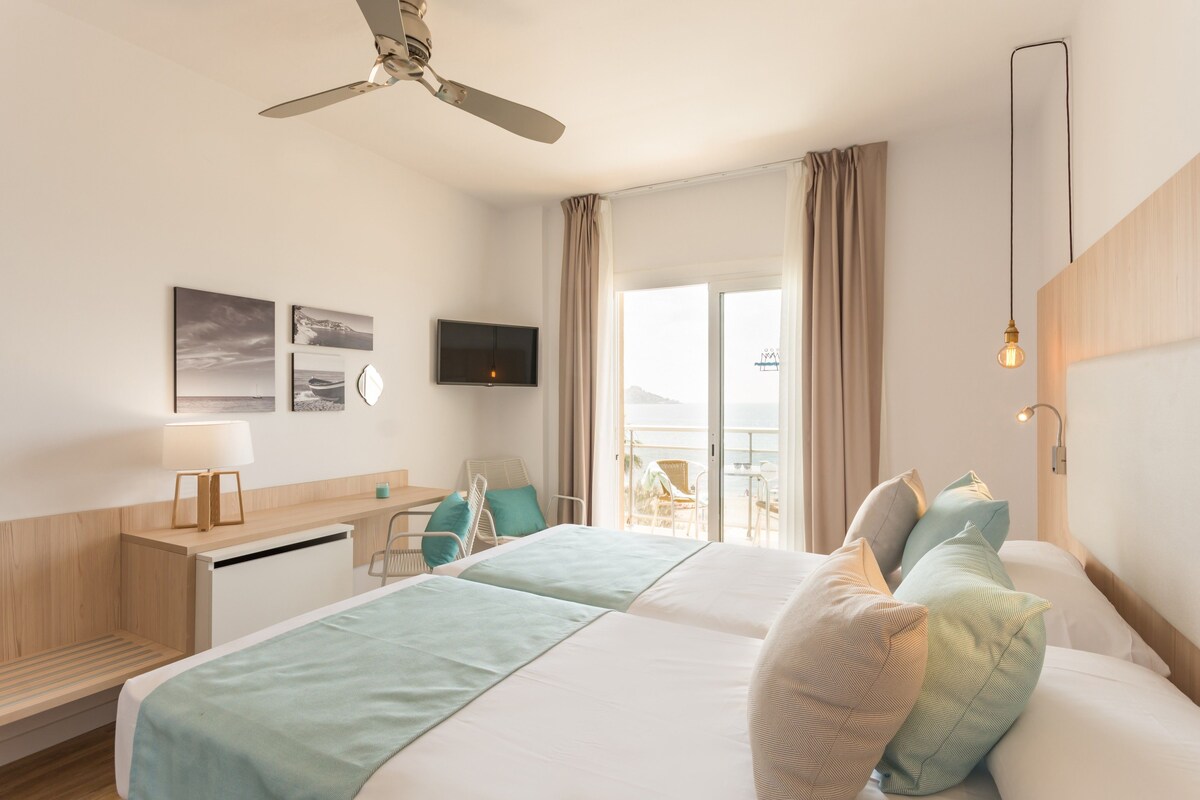 A hotel room with a bed, a desk, a chair, a TV, and a balcony with a view.