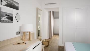 Une chambre d’hôtel moderne avec un bureau en bois, un lit recouvert d’une couverture bleu clair, un radiateur blanc, un miroir et une vue sur le couloir.