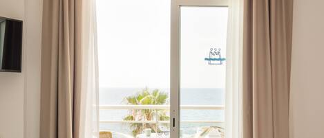 Un dormitorio con cama, una silla, una mesa y vista al océano a través de un ventanal corredero.