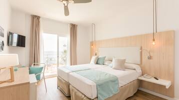 Een hotelkamer met twee bedden, een bureau, een stoel, een televisie en een balkon met gordijnen.