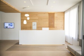 A reception desk with a wooden panel wall, a flat-screen TV, and a modern pendant light. - Hotel Monterrey Roses by Pierre & Vacances (Roses)
