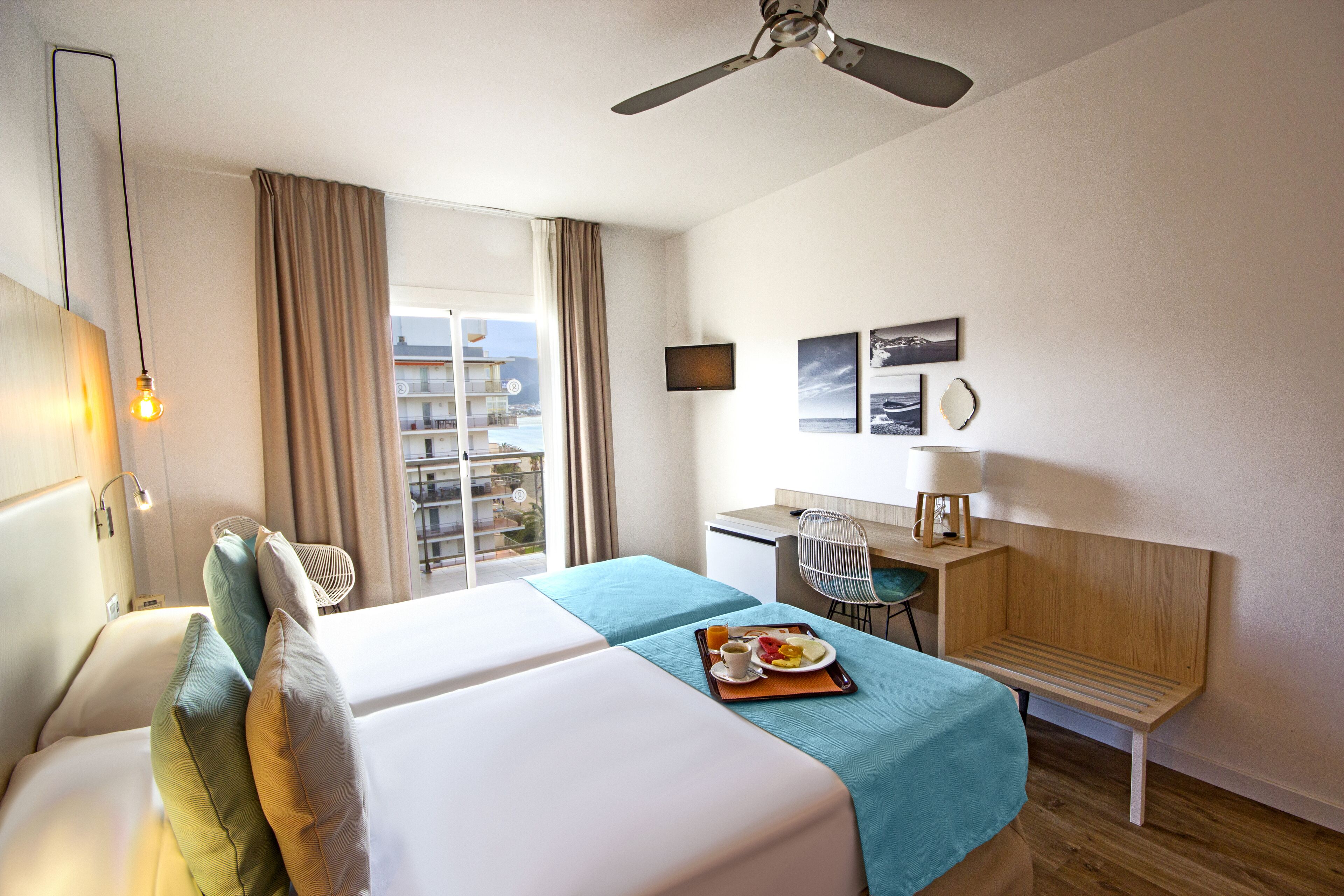 A hotel room with a bed, a desk, a chair, a TV, and a view of the outside.