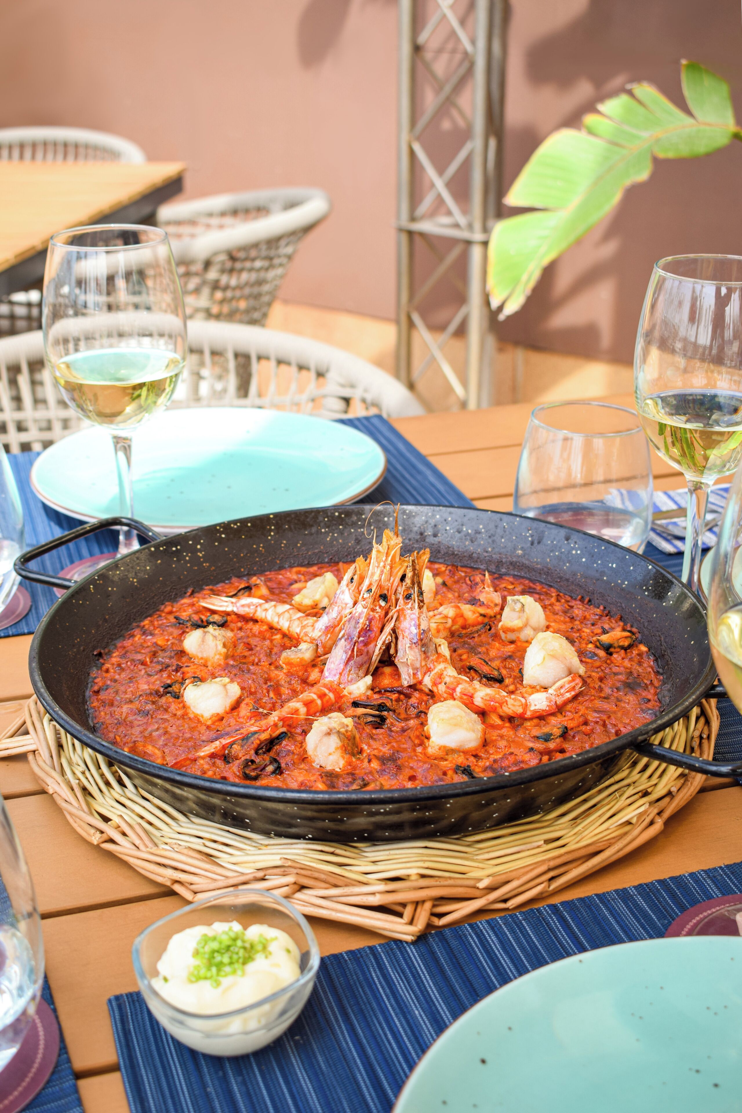 Een eettafel met paella met zeevruchten, een glas witte wijn en een schaal saus.