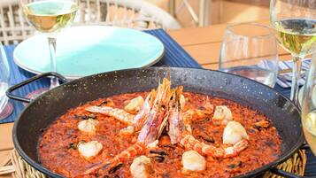 Een eettafel met paella met zeevruchten, een glas witte wijn en een schaal saus.