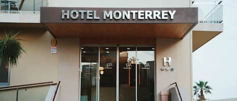 L'entrée de l'hôtel Monterrey se distingue par sa façade moderne, ses portes en verre et un panneau en forme de « H » bien visible, qui indique clairement qu'il s'agit de l'hôtel.