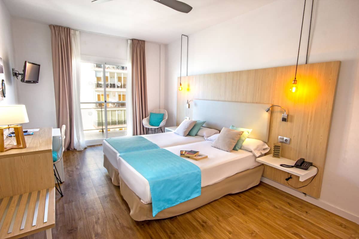 A hotel room with a large bed, a desk with a lamp, a chair, and a view of the outside balcony.
