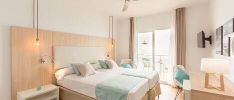 A hotel room with a large bed, bedside tables, a desk with a lamp, a ceiling fan, and a window with curtains.
