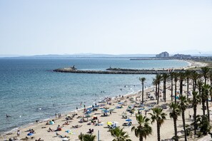 A beach with palm trees, umbrellas, and people. - Hotel Monterrey Roses by Pierre & Vacances (Roses)