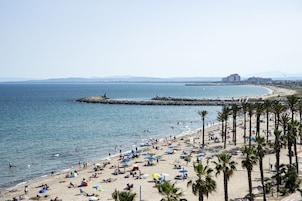 Ein Strand mit Palmen, Sonnenschirmen und Menschen.