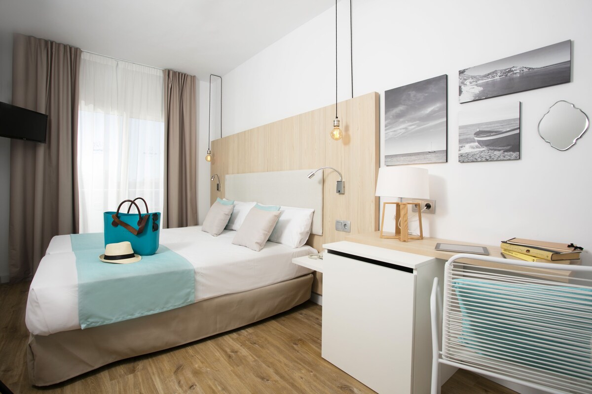 A modern hotel room with a bed, bedside table, lamp, and artwork on the wall.