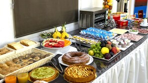 Un bufé con diversas opciones de comida, como frutas, bollería y bebidas.
