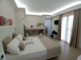 Habitación de hotel con una cama litera, un escritorio, un televisor de pantalla plana y un ventanal con cortinas.