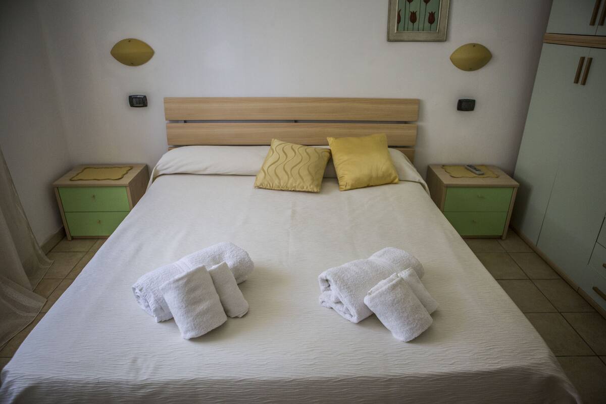 A neatly made bed with two pillows, two bedside tables, and a green nightstand.
