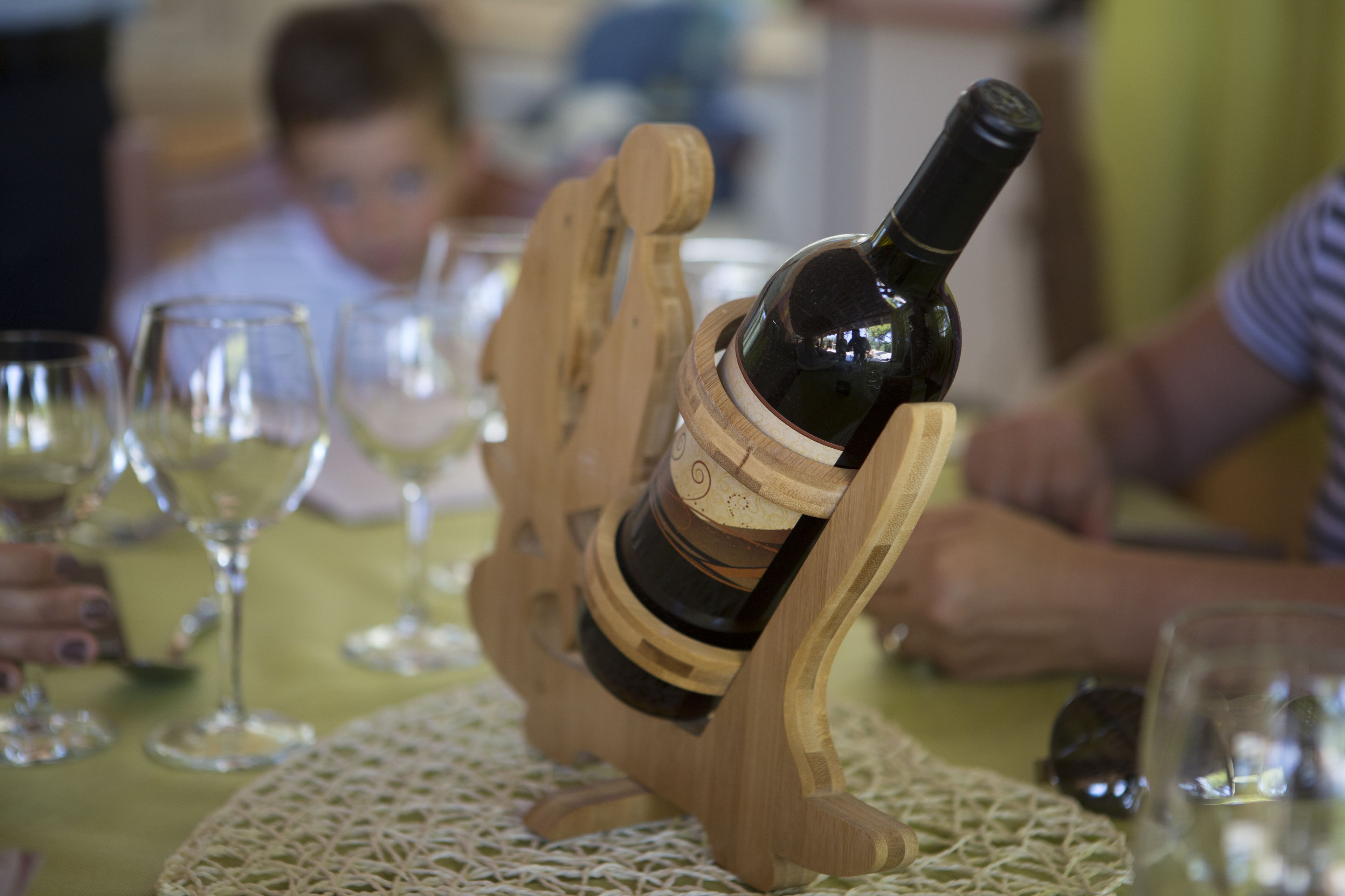 A bottle of wine on a wooden stand with glasses around it.