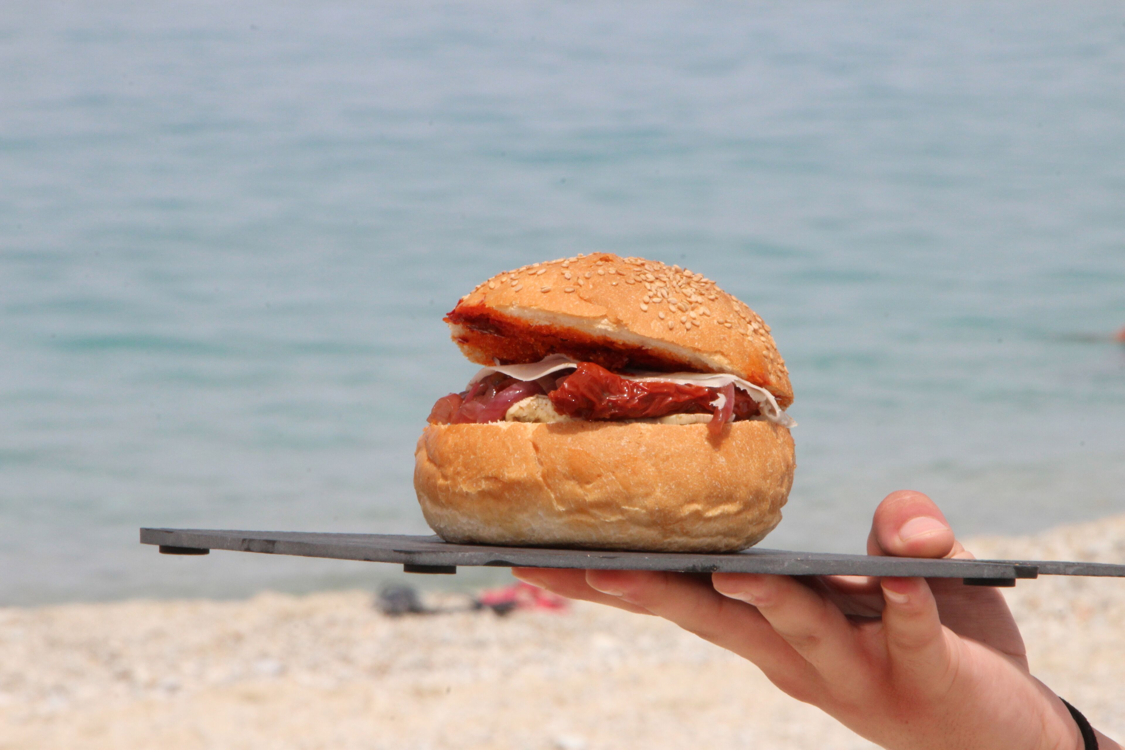 A hand holding a sandwich over a beach.