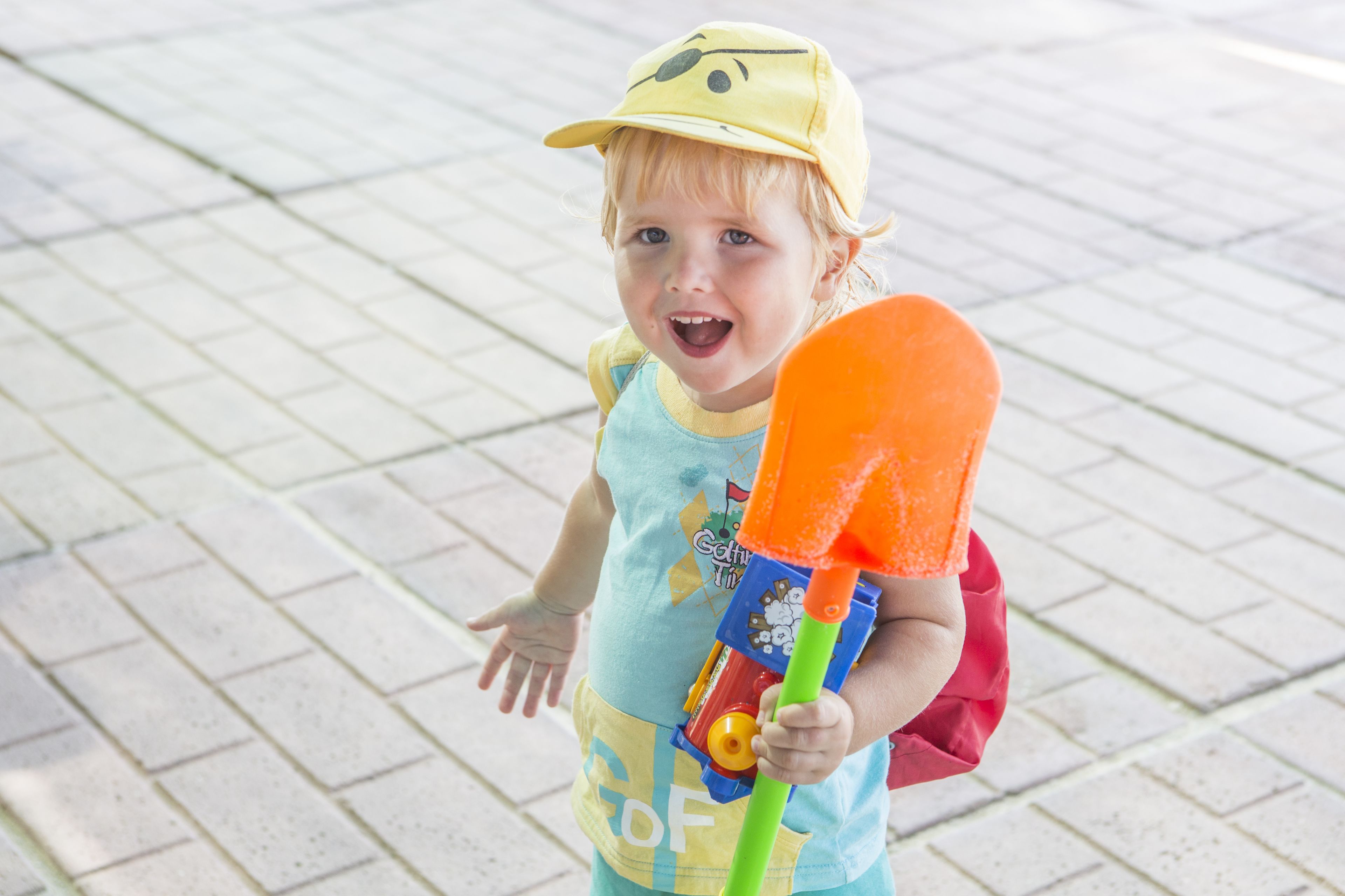 A child holding a toy shovel and wearing a cap.