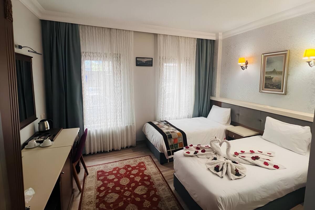A hotel room with two beds, a desk, a chair, a coffee maker, and a red patterned rug.
