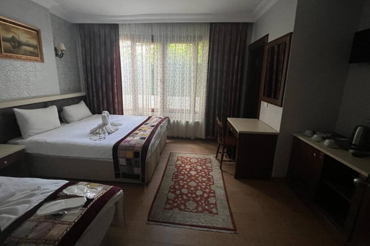 A hotel room with a bed, a desk, a chair, a TV, and a window with curtains.