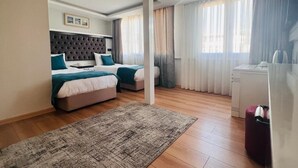 Ein Hotelzimmer mit einem großen Bett, einem kleineren Bett, einem Schreibtisch und einem Sessel.