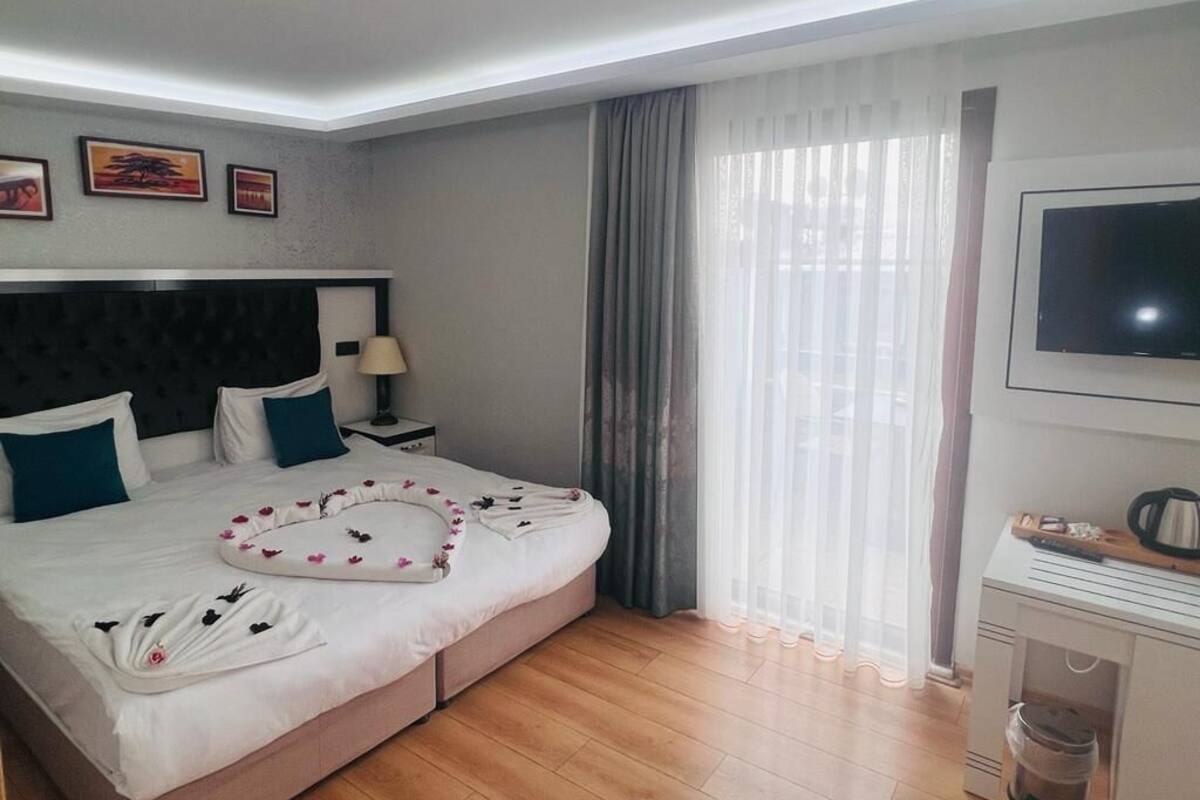 A hotel room with a bed, a TV, a desk, and a window with curtains.