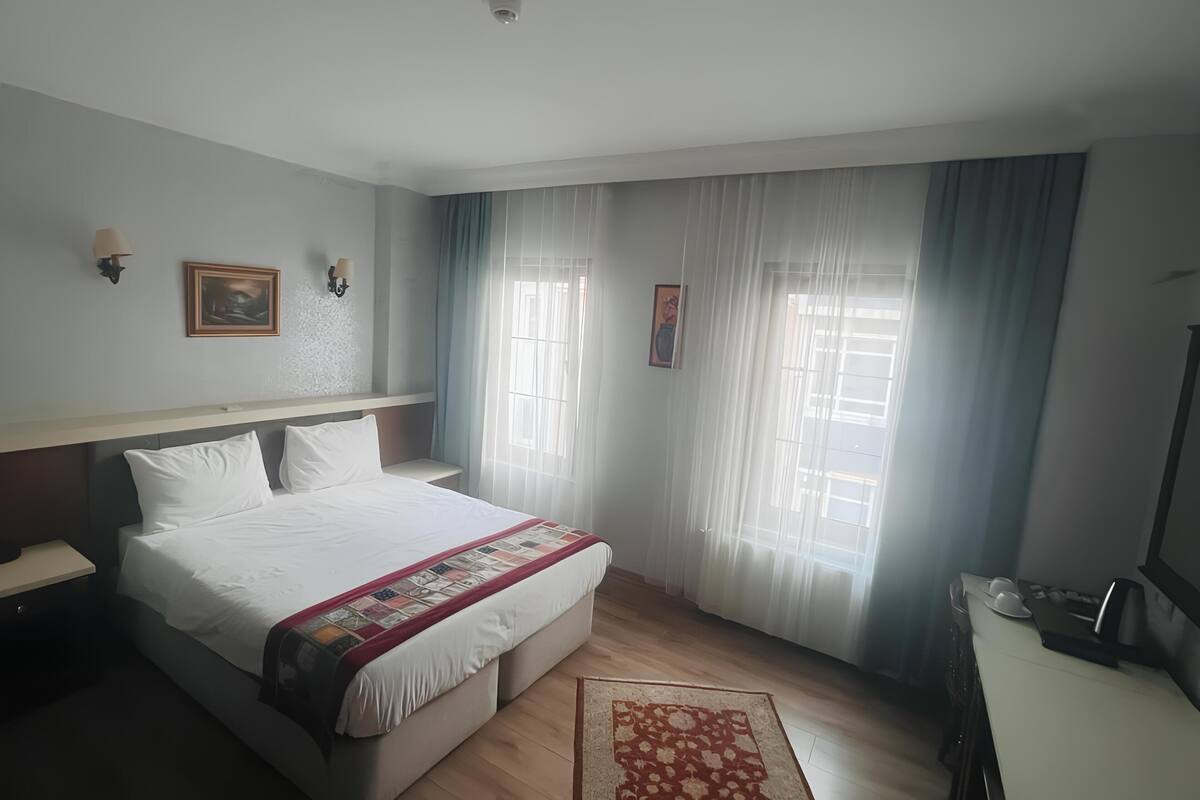 A hotel room with a bed, a desk, a chair, a TV, and a window with curtains.