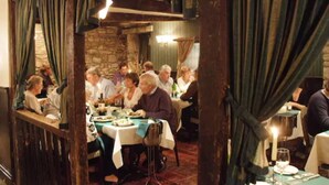 Zona pranzo con tavoli rotondi, travi in legno e tende verdi.