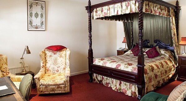 A four-poster bed with floral bedding, a matching chair, a desk with a lamp, and a framed picture on the wall. - The Bear Hotel, Crickhowell (Crickhowell)