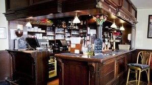Zona bar con arredi in legno, scaffali pieni di bottiglie e una lavagna con il menu.