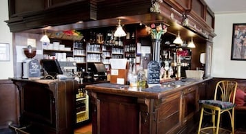 Zona de bar con mobiliario de madera, estantes llenos de botellas y un menú en una pizarra.