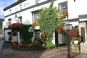 A white building with the name "The Bear" on the facade, featuring a brick pathway, flower boxes, and a green ivy-covered wall. - The Bear Hotel, Crickhowell (Crickhowell)