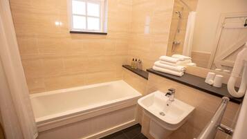 A bathroom with a bathtub, a sink, a window, and a shower.