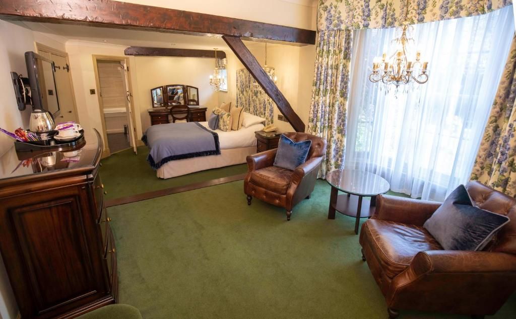 Una habitación de hotel con una cama, dos sillones de cuero, una mesita, un armario de madera y una araña.