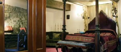 A four-poster bed with a canopy, a stone wall, and a green sofa in a room with a wooden floor.