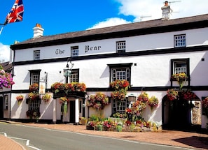 A white building with the name "The Bear" on the facade, featuring multiple windows and flower baskets. - The Bear Hotel, Crickhowell (Crickhowell)