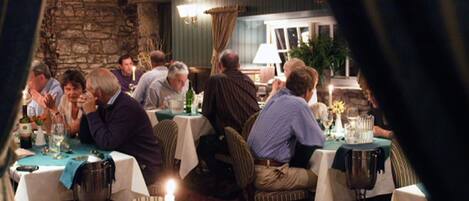 A restaurant with multiple tables, candles, and a stone wall in the background.