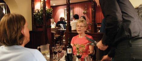 L’intérieur d’un restaurant, avec des meubles en bois, un coin bar et une table à manger agrémentée de verres et de bouteilles de vin.