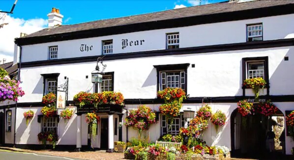 A white building with the name "The Bear" on the facade, featuring multiple windows and hanging flower baskets. - The Bear Hotel, Crickhowell (Crickhowell)