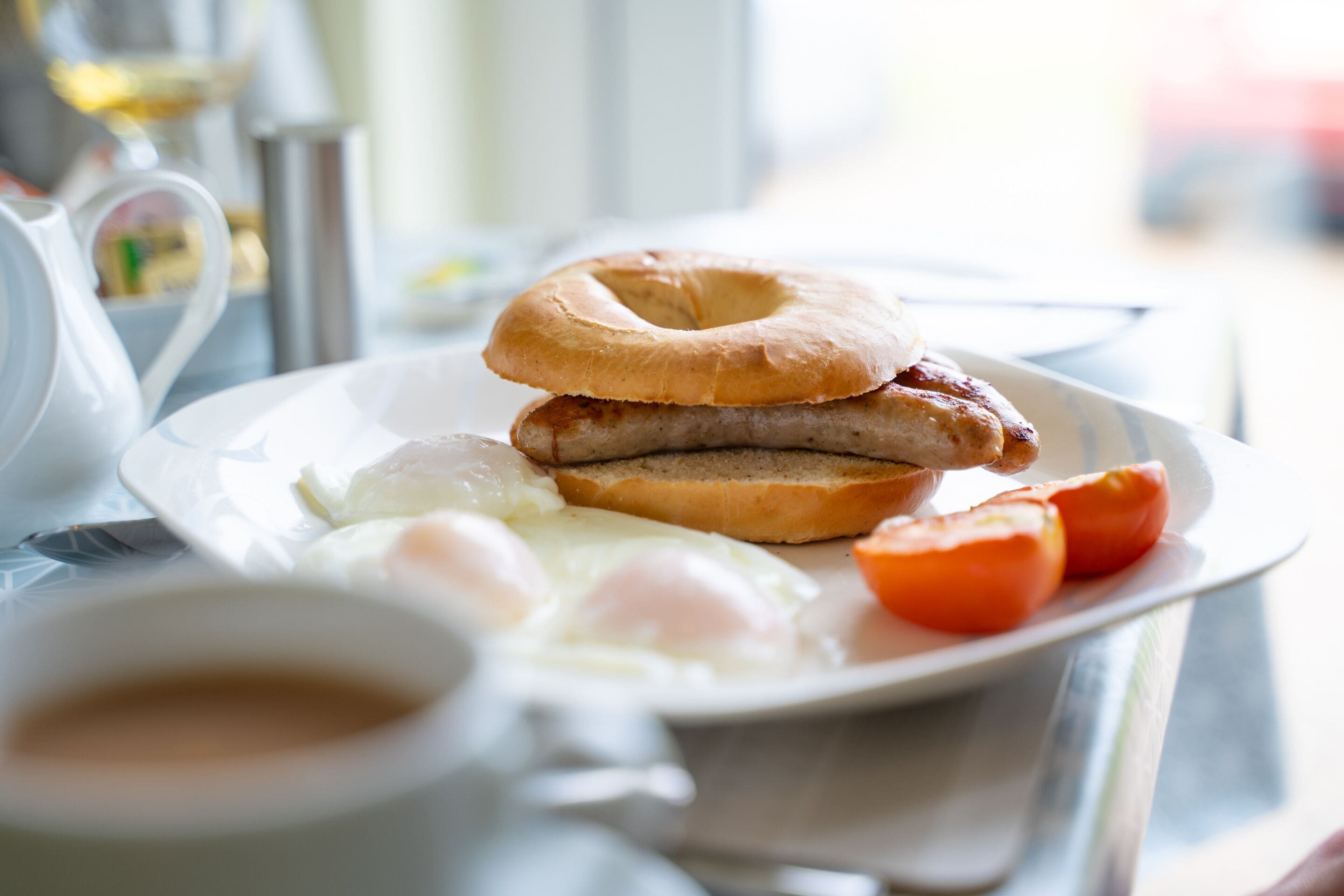 A breakfast plate with a bagel, sausage, eggs, and tomatoes.