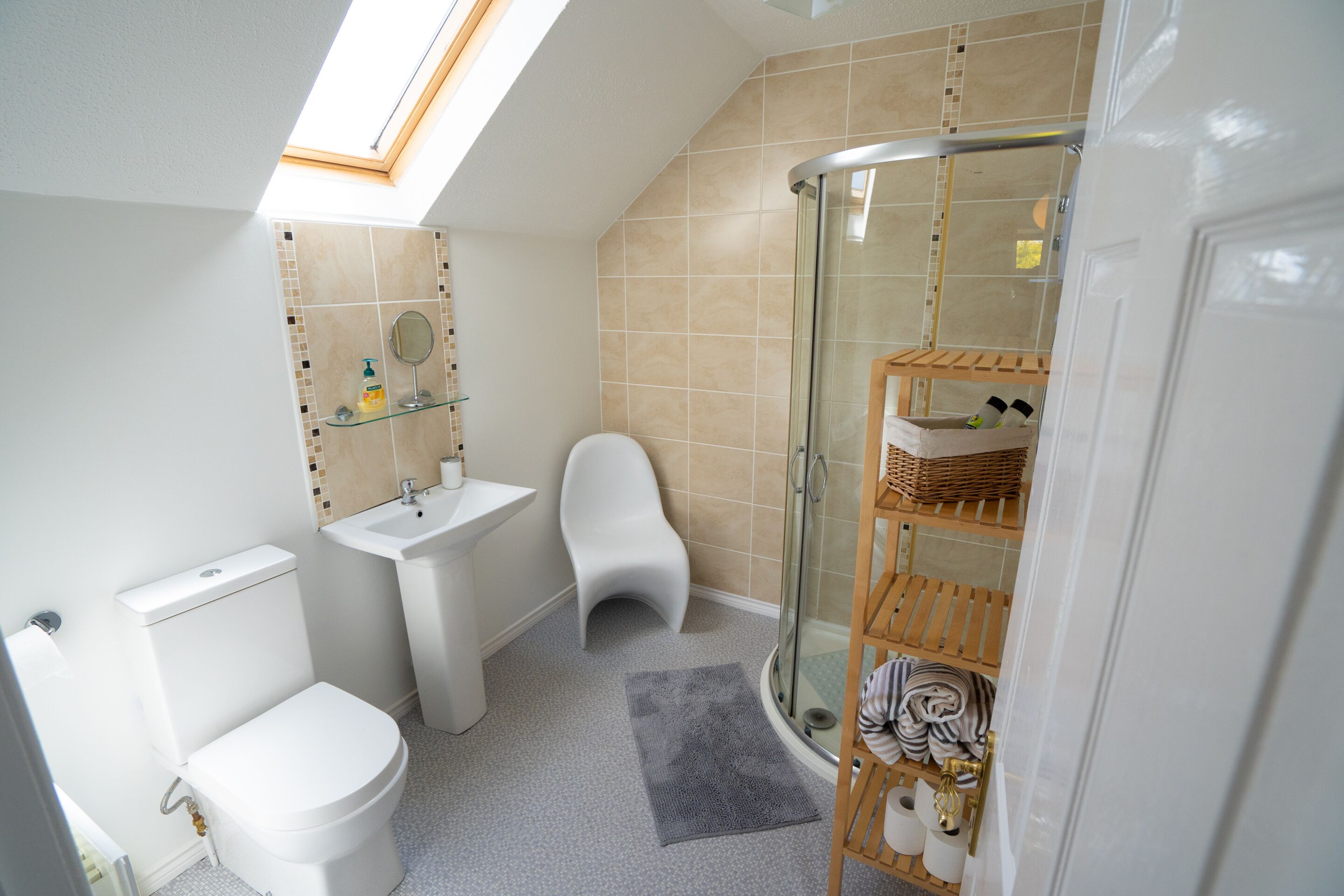 Een moderne badkamer met dakraam, toilet, wastafel, douche en een houten plank met handdoeken.