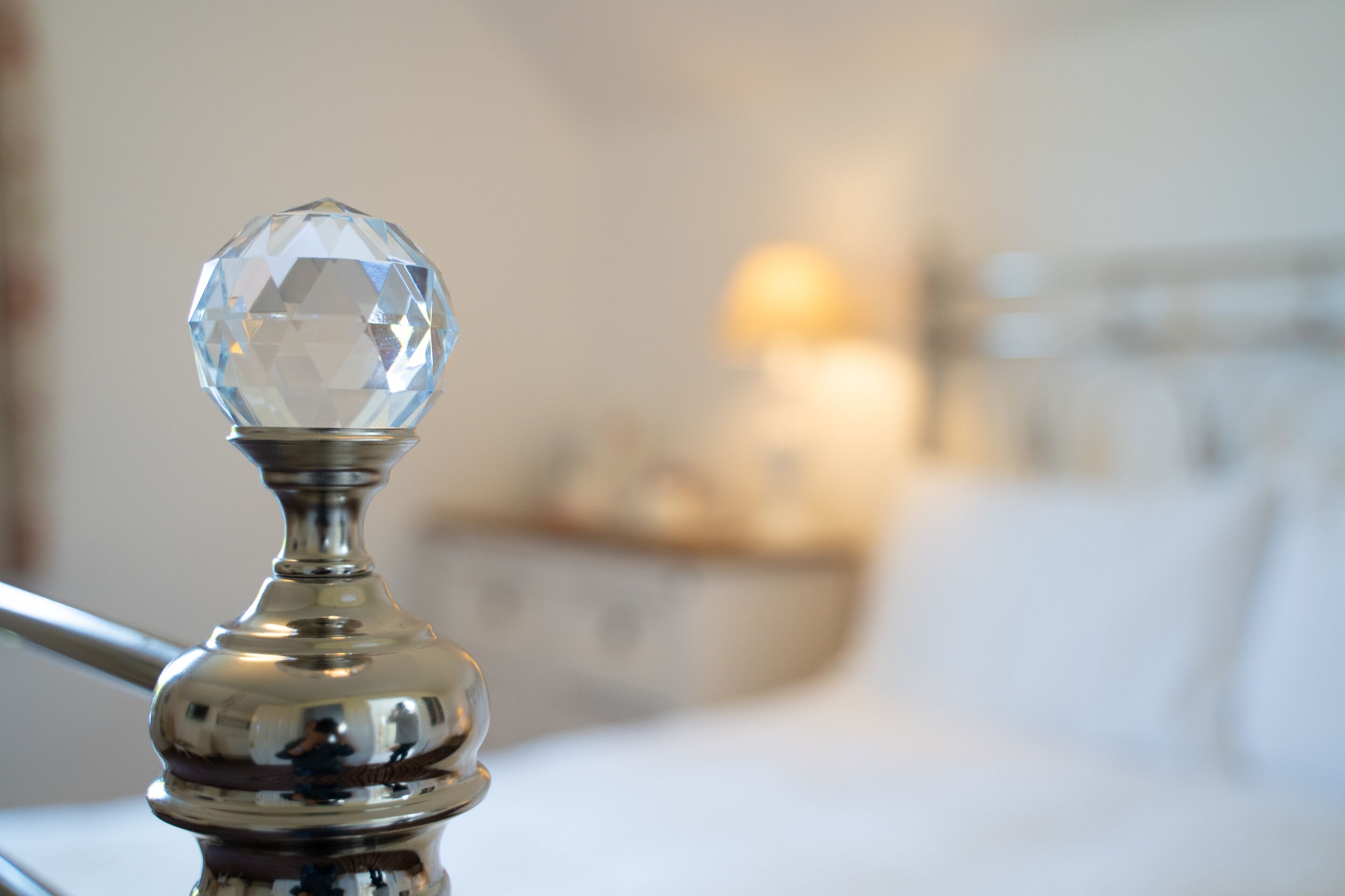 A close-up of a crystal-adorned metal fixture, likely part of a bed frame, with a blurred background suggesting a well-lit room.