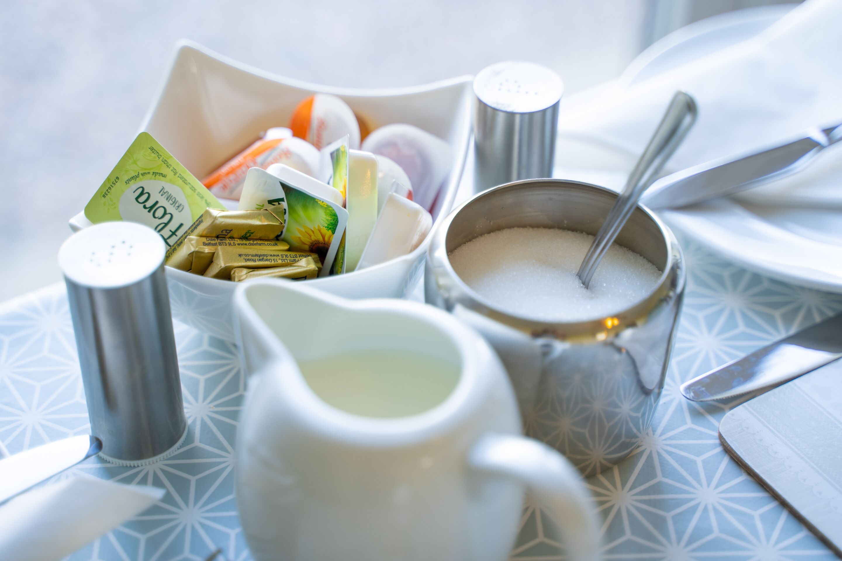 A table setting with a salt shaker, sugar bowl, and a white pitcher.
