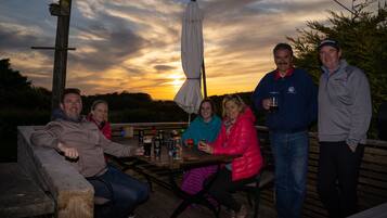 A group of people seated at a wooden table outdoors with a sunset in the background.