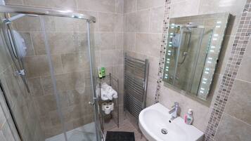 A modern bathroom with a glass-enclosed shower, a white sink, and a mirror with lights.