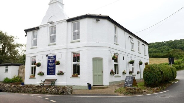 A white building with a green door, labeled as "The Herd Inn." - The Highdown Inn (Totland Bay)