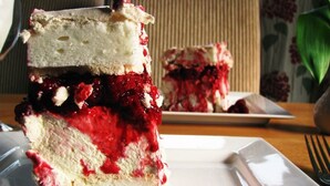 A slice of layered cake with a red fruit topping on a white plate. - The Highdown Inn (Totland Bay)