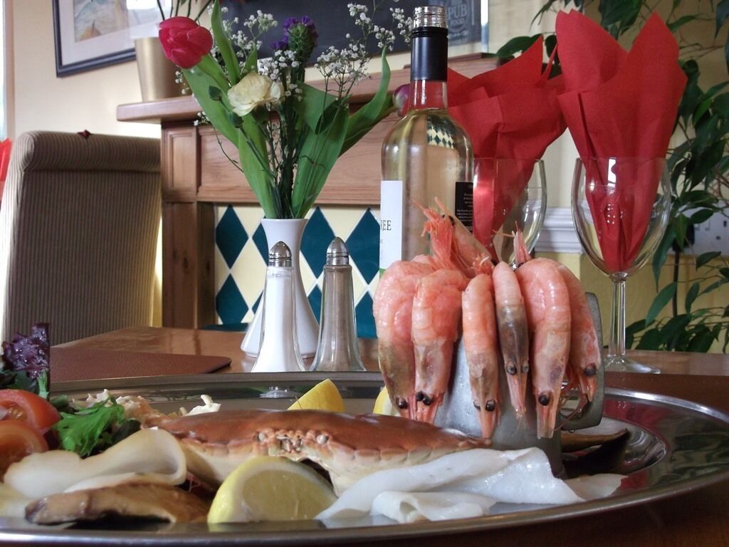 A seafood platter with shrimp, oysters, and other seafood on a tray, accompanied by a bottle of white wine and a glass of red wine.