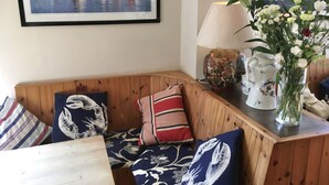 A cozy corner with a wooden bench, a framed painting of sailboats, a lamp, and a vase with flowers. - The Highdown Inn (Totland Bay)